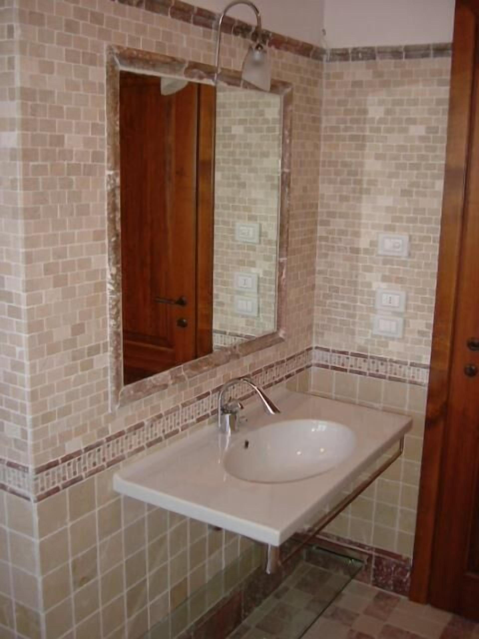 Un baño con un lavamanos rectangular, un espejo y paredes con azulejos.
