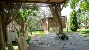 Una recepción de boda al aire libre con mesas redondas cubiertas con manteles blancos, sillas y copas.