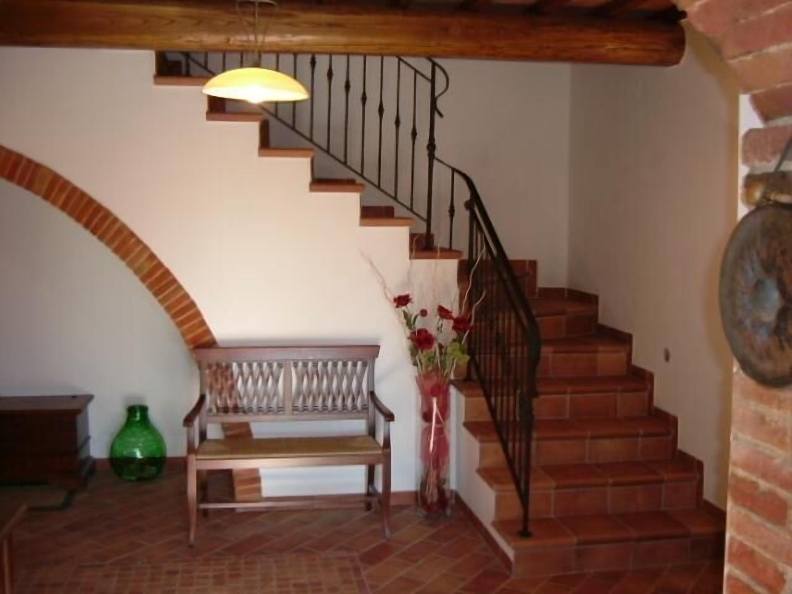 A staircase with a wooden handrail and a metal railing, a bench, and a vase with flowers.