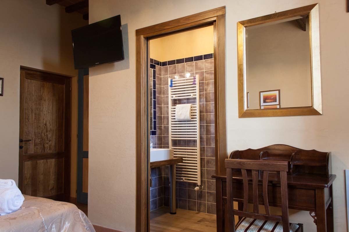 Ein Zimmer mit einem Bett, einem Holzstuhl, einem Fernseher sowie einem Badezimmer inklusive Handtuchhalter und Spiegel.