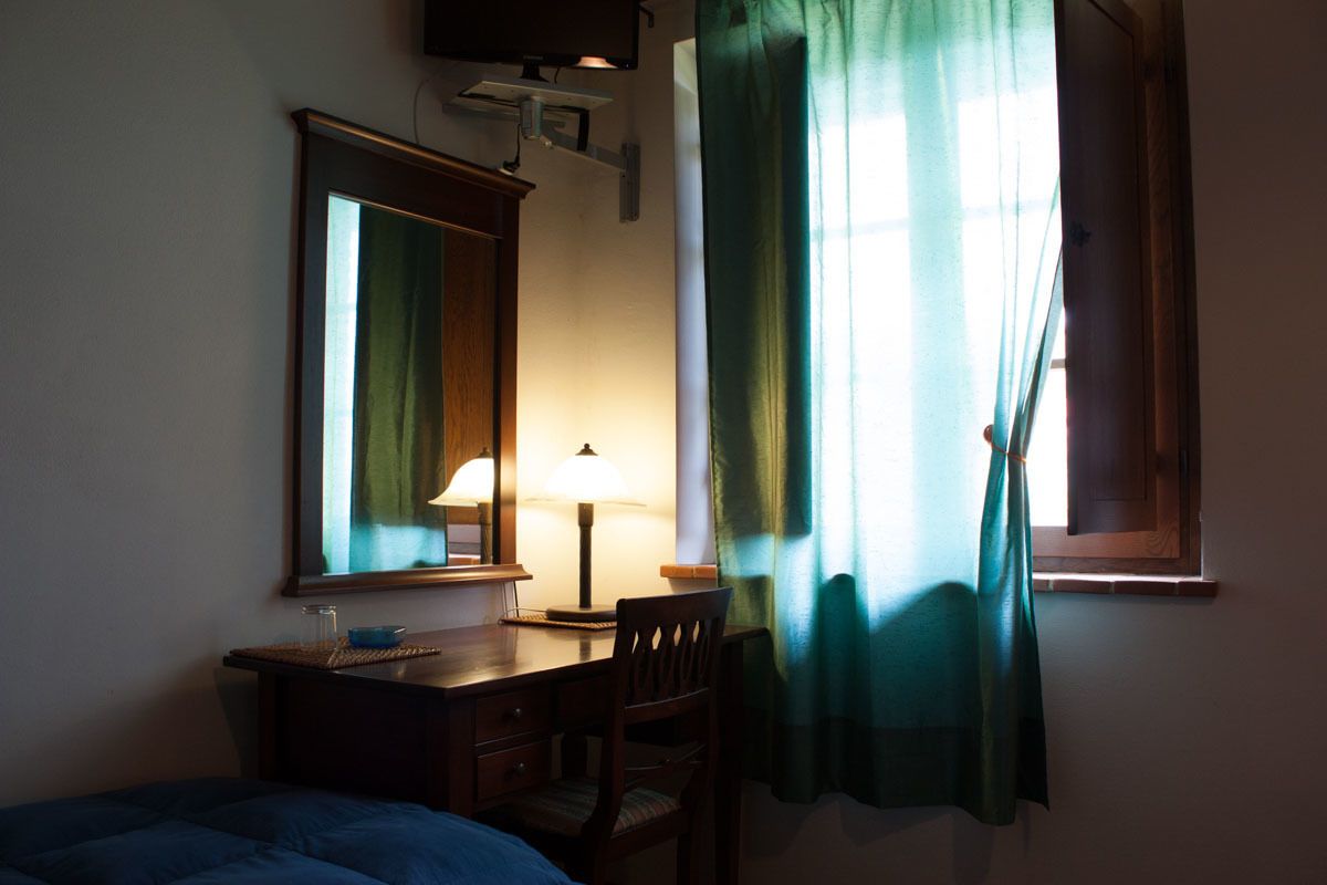 A room with a bed, a desk with a lamp, a chair, a mirror, and a window with curtains.