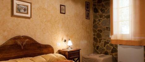 Un dormitorio acogedor con cabecera de madera, lámpara de noche, una mesita y pared de piedra.