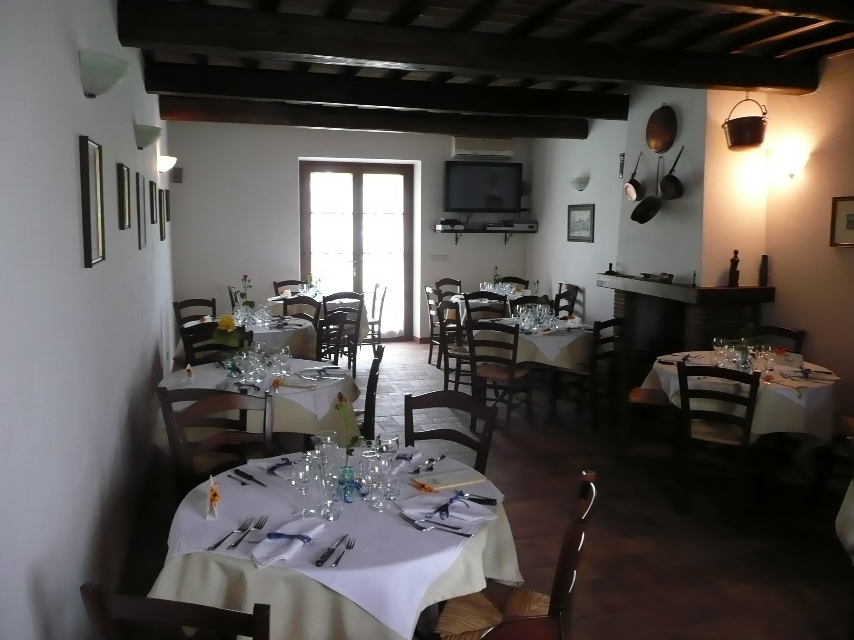 A dining area with multiple tables set for meals, a television mounted on the wall, and a fireplace with a hanging pot.