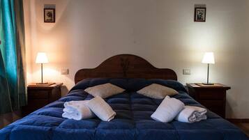 Una cama bien hecha con un edredón azul oscuro y varias toallas dobladas. Hay dos mesitas de noche con lámparas, y la habitación tiene un diseño sencillo y limpio.