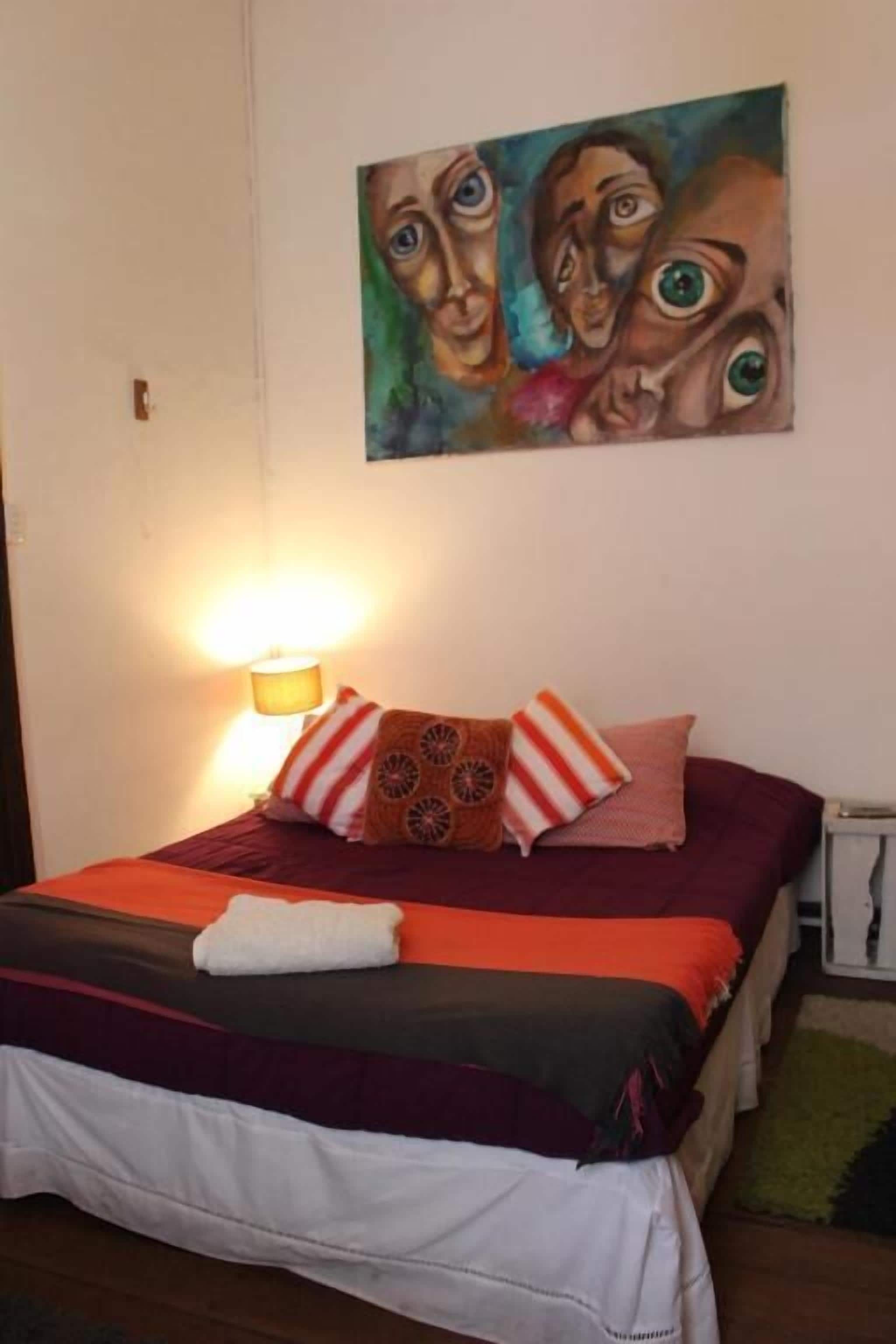 Un dormitorio con una cama, almohadas, un cuadro en la pared y una lámpara.