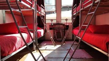A dormitory room with bunk beds, a small table, and a view through the windows.