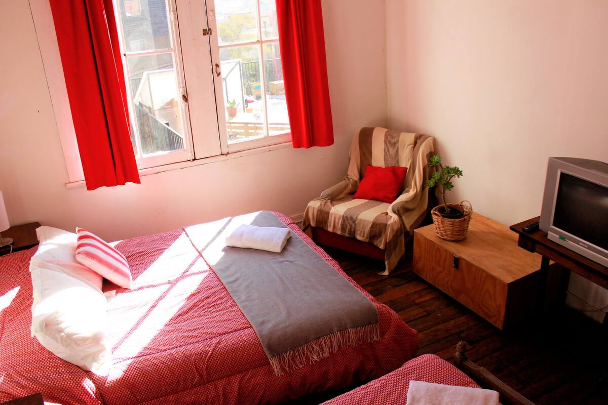 Une chambre à coucher avec un lit, une chaise, un téléviseur et une fenêtre avec des rideaux.