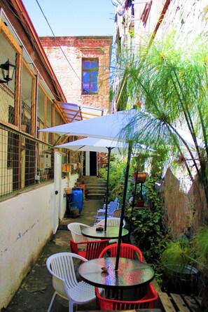 An outdoor patio area with tables and chairs, surrounded by plants and a brick building. - Casa Volante Hostal - Hostel (Valparaiso)