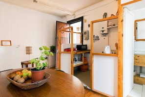 A kitchen with a wooden table, a bowl of fruit, a potted plant, and a gas cylinder.