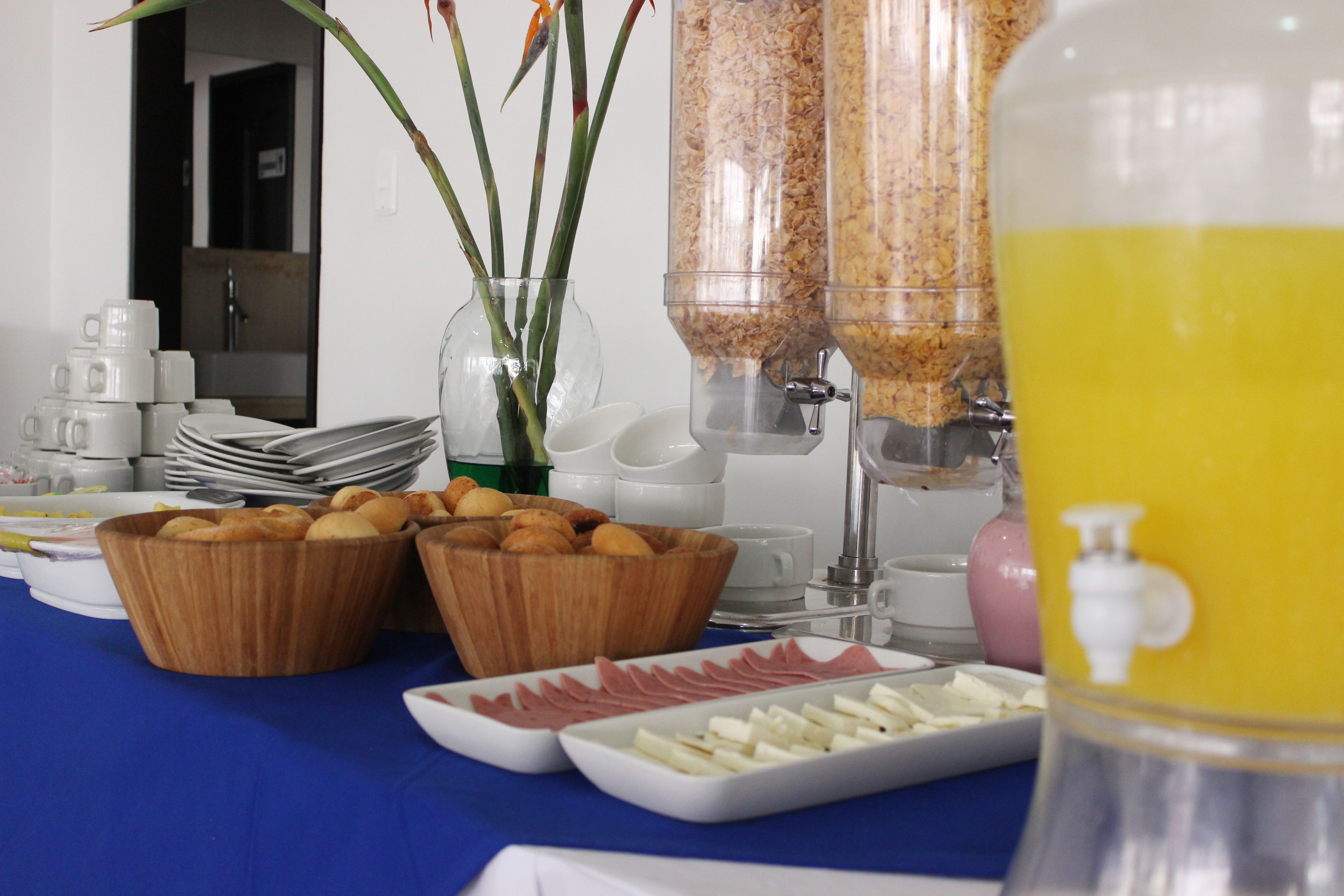 Una mesa de buffet con diversos alimentos, incluyendo tazones de pastelería y fiambres, además de un dispensador de bebidas.