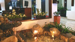 Un área de recepción con una fuente de piedra, plantas en macetas y un mostrador de recepción.