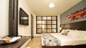 Una habitación de hotel con una cama, un escritorio con televisión de pantalla plana, un adorno en la pared y un ventanal con diseño de celosía.