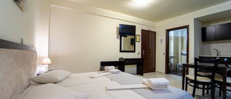 Habitación de hotel con cama, escritorio, silla, televisor y baño visible a través de una puerta abierta.
