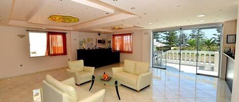 A spacious living room with a large glass door leading to a balcony, white sofas, and a small coffee table.