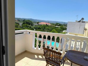 A balcony with a view of a swimming pool, a chair, and a table. - Golden Rose Suites (Platanias)