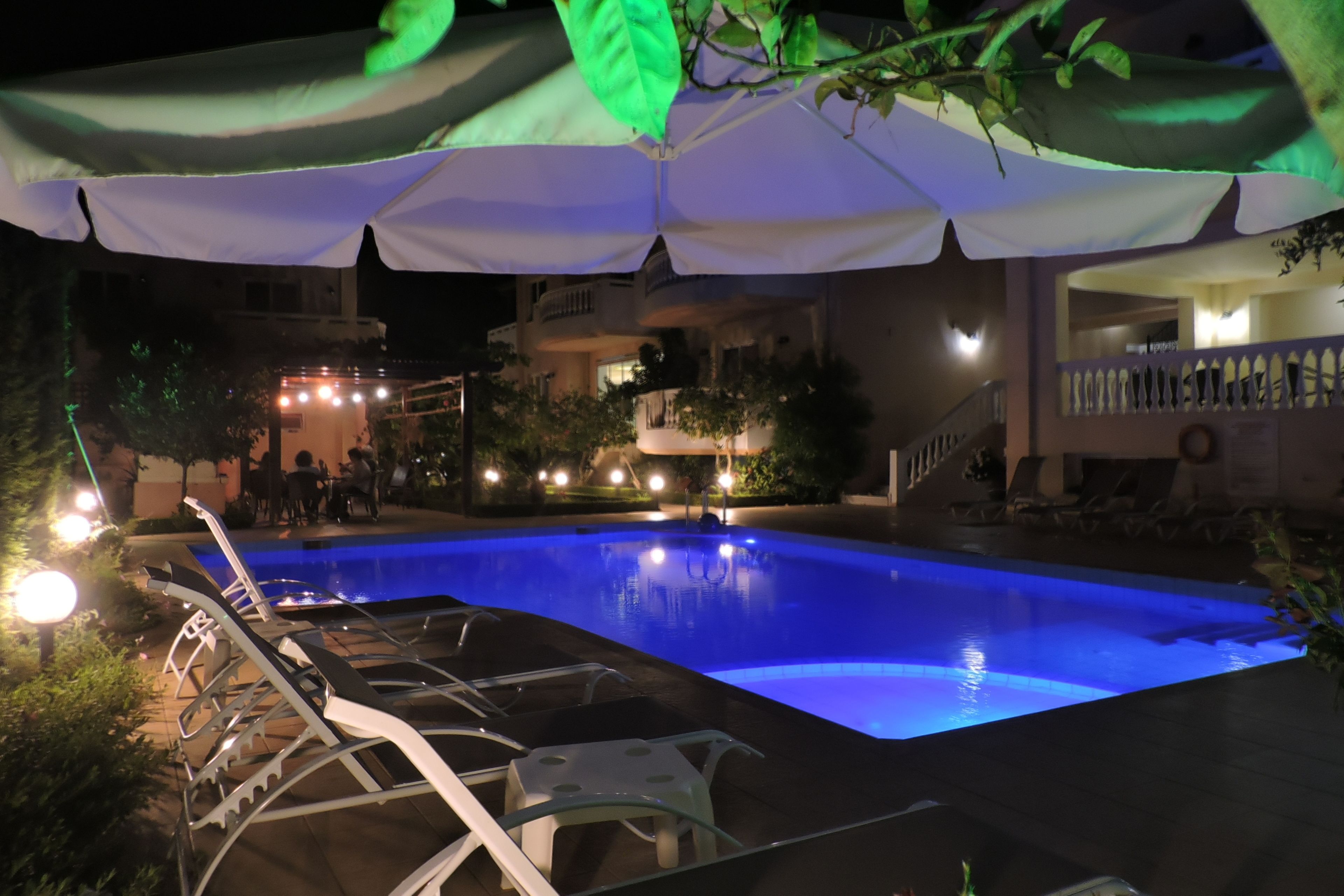 Area piscina illuminata di notte con poltrone a sdraio e ombrelloni.