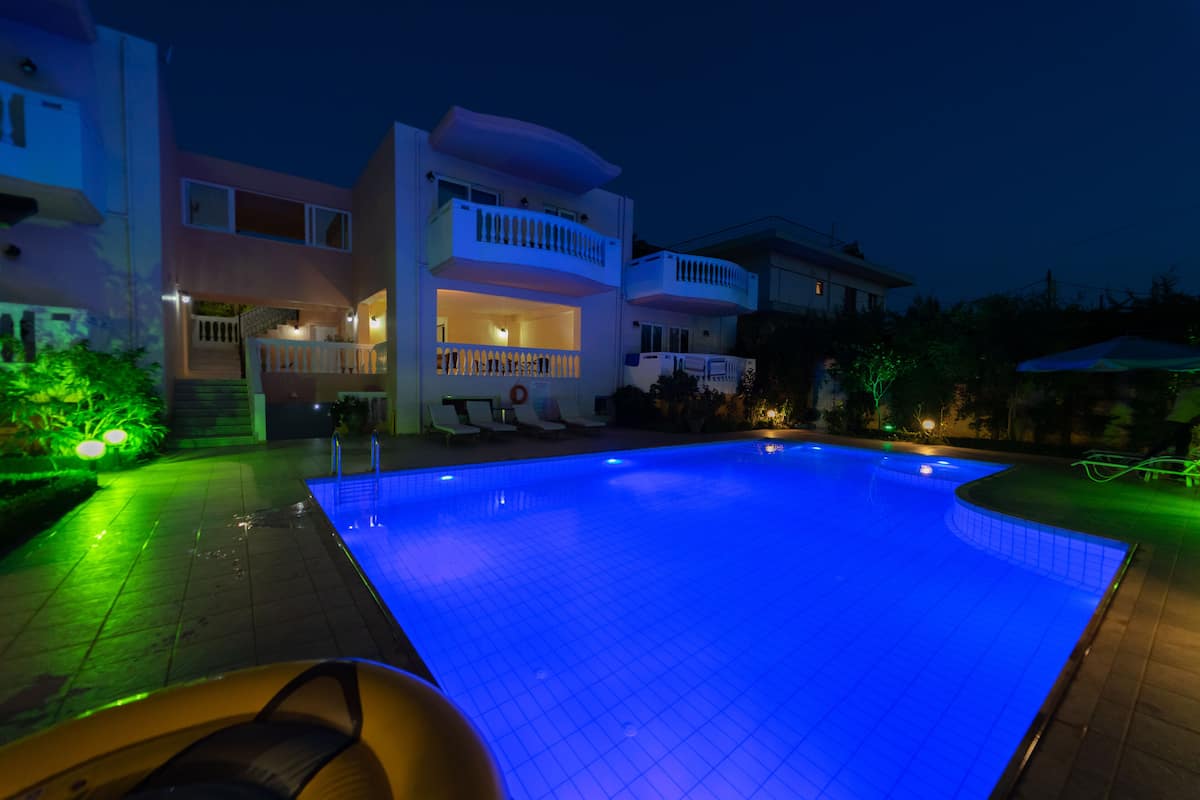A swimming pool with a blue-lit water feature, surrounded by a multi-story building with balconies and outdoor seating.