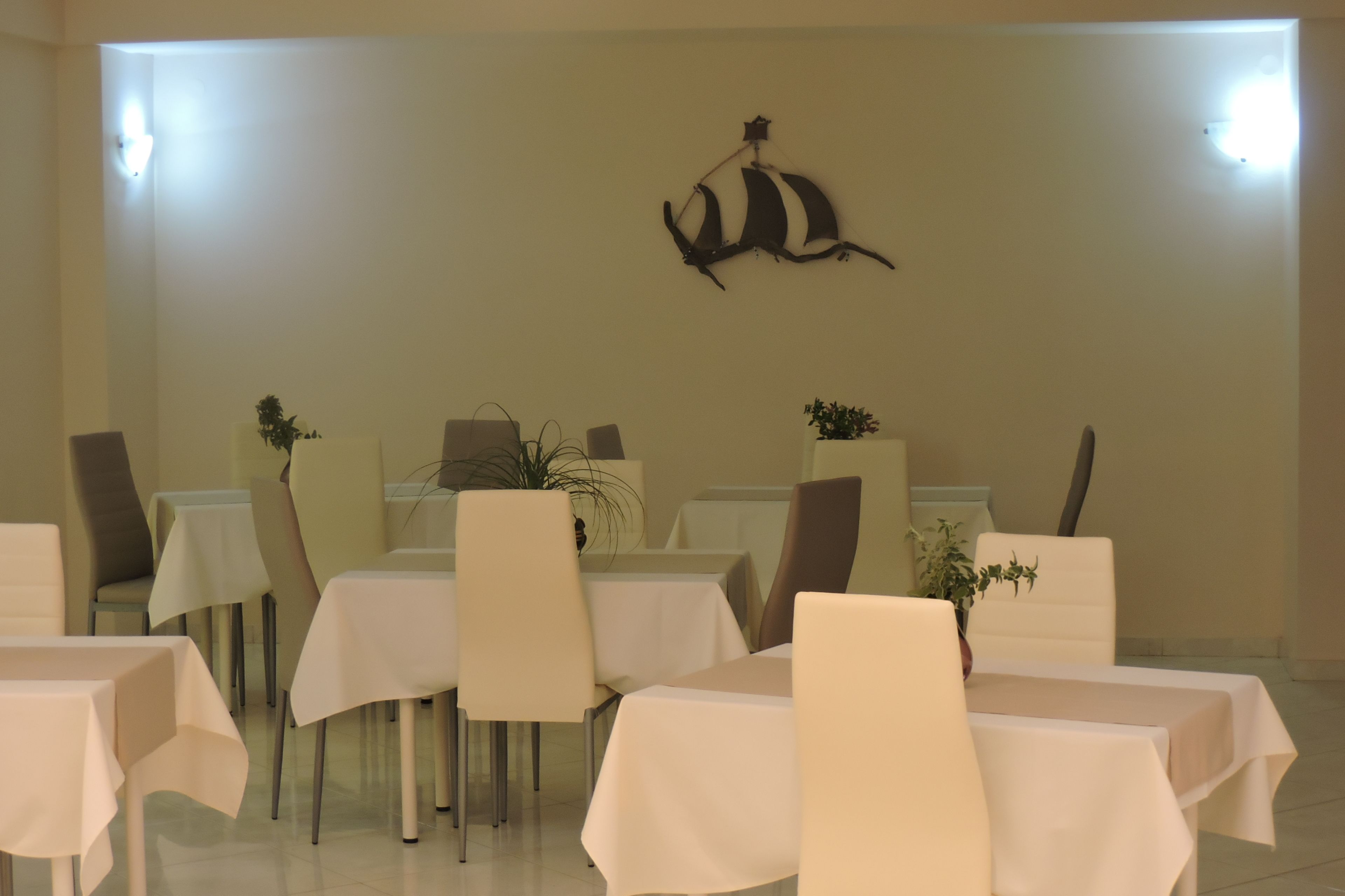 Un comedor con mesas y sillas, un adorno en la pared y plantas en macetas.