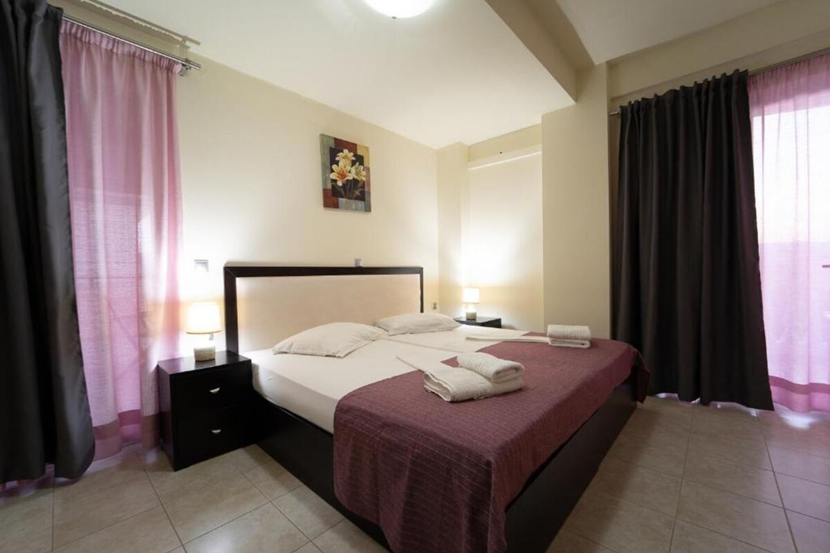 Una habitación de hotel con cama, mesitas de noche, un cuadro en la pared y cortinas.