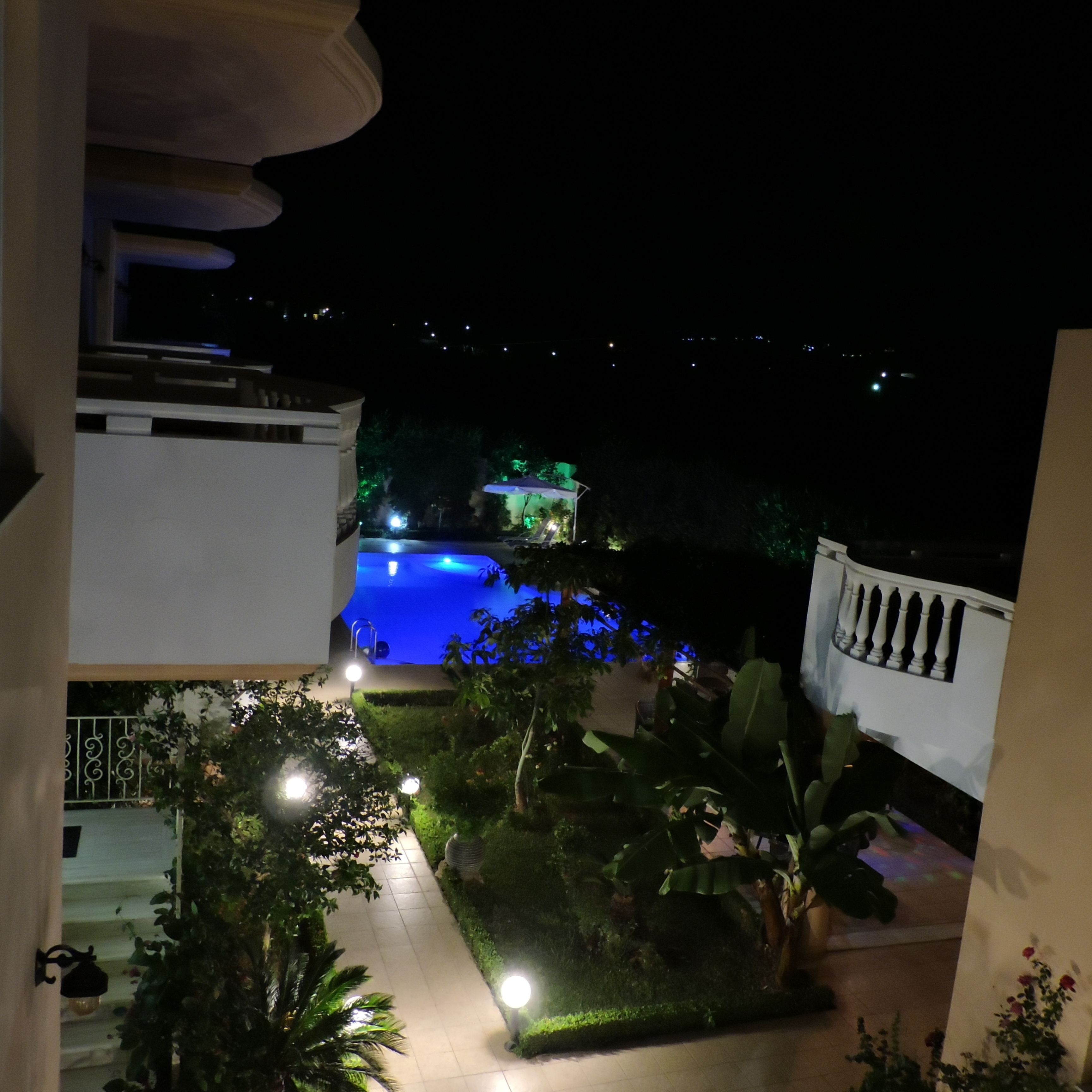 A nighttime view of a swimming pool with surrounding greenery and a balcony.