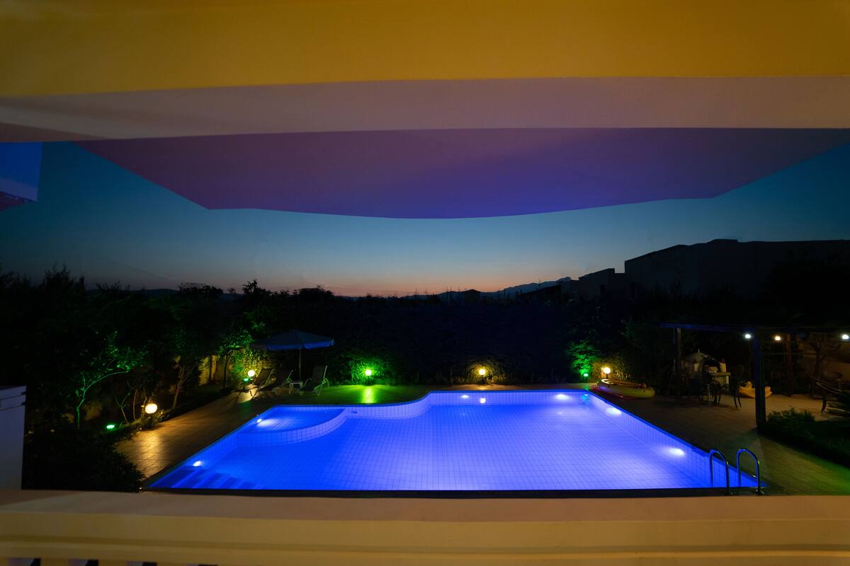 A swimming pool at dusk with surrounding lights and a view of buildings in the background.