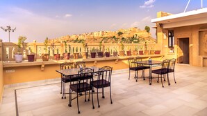 A terrace with a table and chairs, potted plants, and a view of a cityscape. - Hotel Sky Plaza (Jaisalmer)