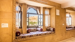 A room with a built-in bench along a wall, a large mirror, and a window with an open door. - Hotel Sky Plaza (Jaisalmer)