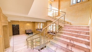 A grand staircase with marble steps and metal railings, leading to a second floor with a large window and a bench. - Hotel Sky Plaza (Jaisalmer)