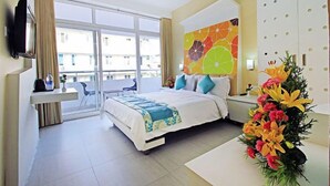 Una habitación de hotel con cama, escritorio, televisor, ventana y un adorno en la pared.