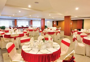 A banquet hall with round tables set for dining, each with white tablecloths and red sashes, and white chairs with red sashes. - Cochin Palace (Kanayannur)