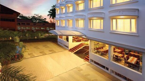 A multi-story hotel with a central staircase, large windows, and a well-lit exterior. - Cochin Palace (Kanayannur)