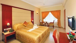 A hotel room with a large bed, a desk, a chair, a television, and a window with curtains. - Cochin Palace (Kanayannur)