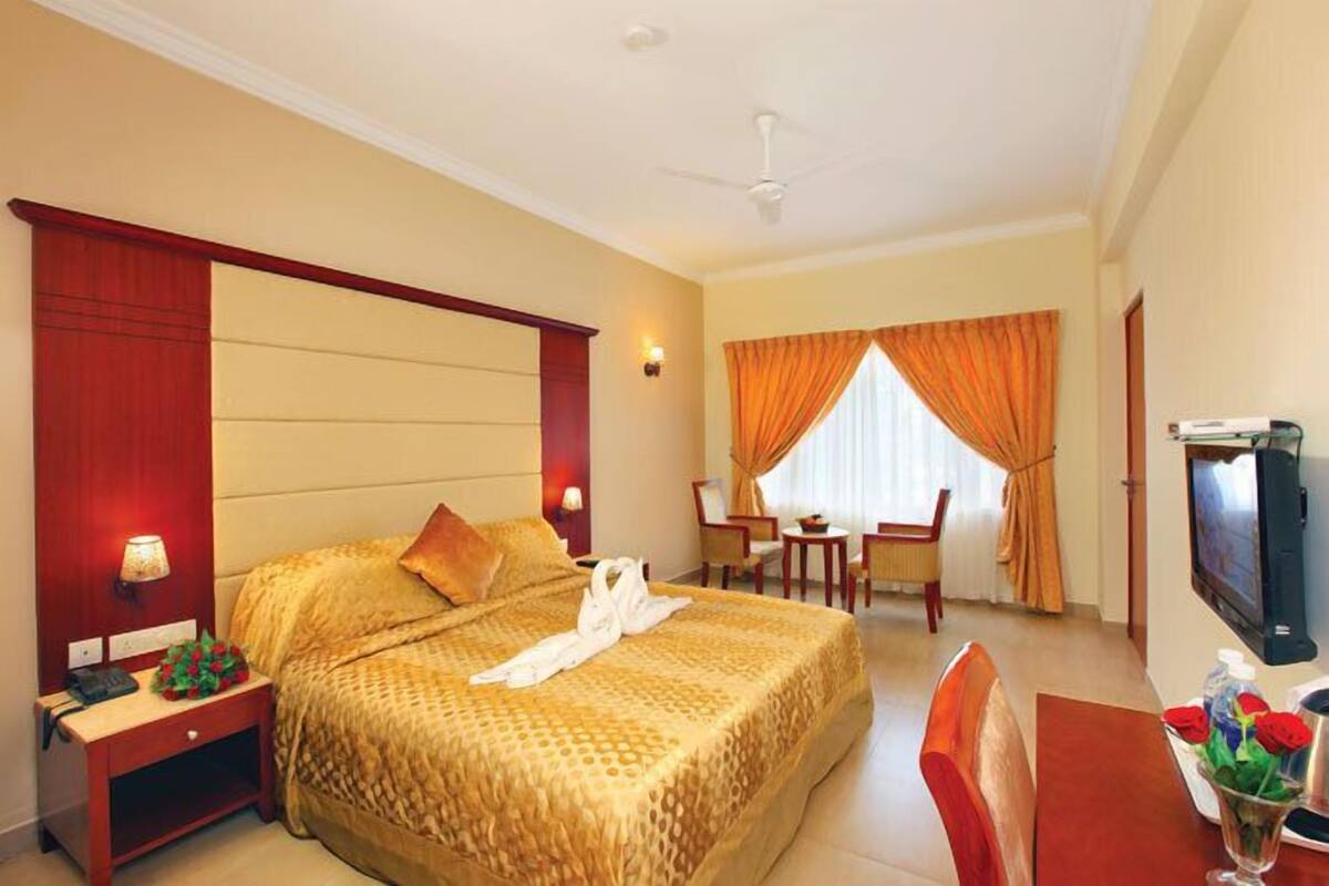 Quarto de hotel com cama grande, escrivaninha, cadeira, televisão e janela com cortinas.