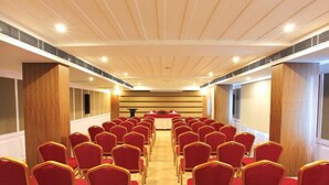 A conference room with rows of red chairs and a long table at the front. - Cochin Palace (Kanayannur)