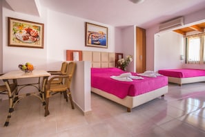 A hotel room with two beds, a dining table with chairs, and a fruit bowl. - Mariamare apts (Hersonissos)