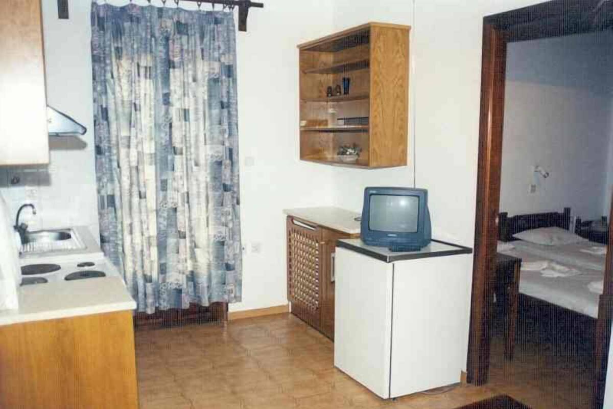 Eine kleine Küche mit Spüle, Herd und einem kleinen Kühlschrank. Darüber befindet sich ein Holzschrank und ein Fernseher steht darauf.