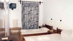 Une chambre avec deux lits en bois, une petite table, un téléviseur fixé au mur et un radiateur.