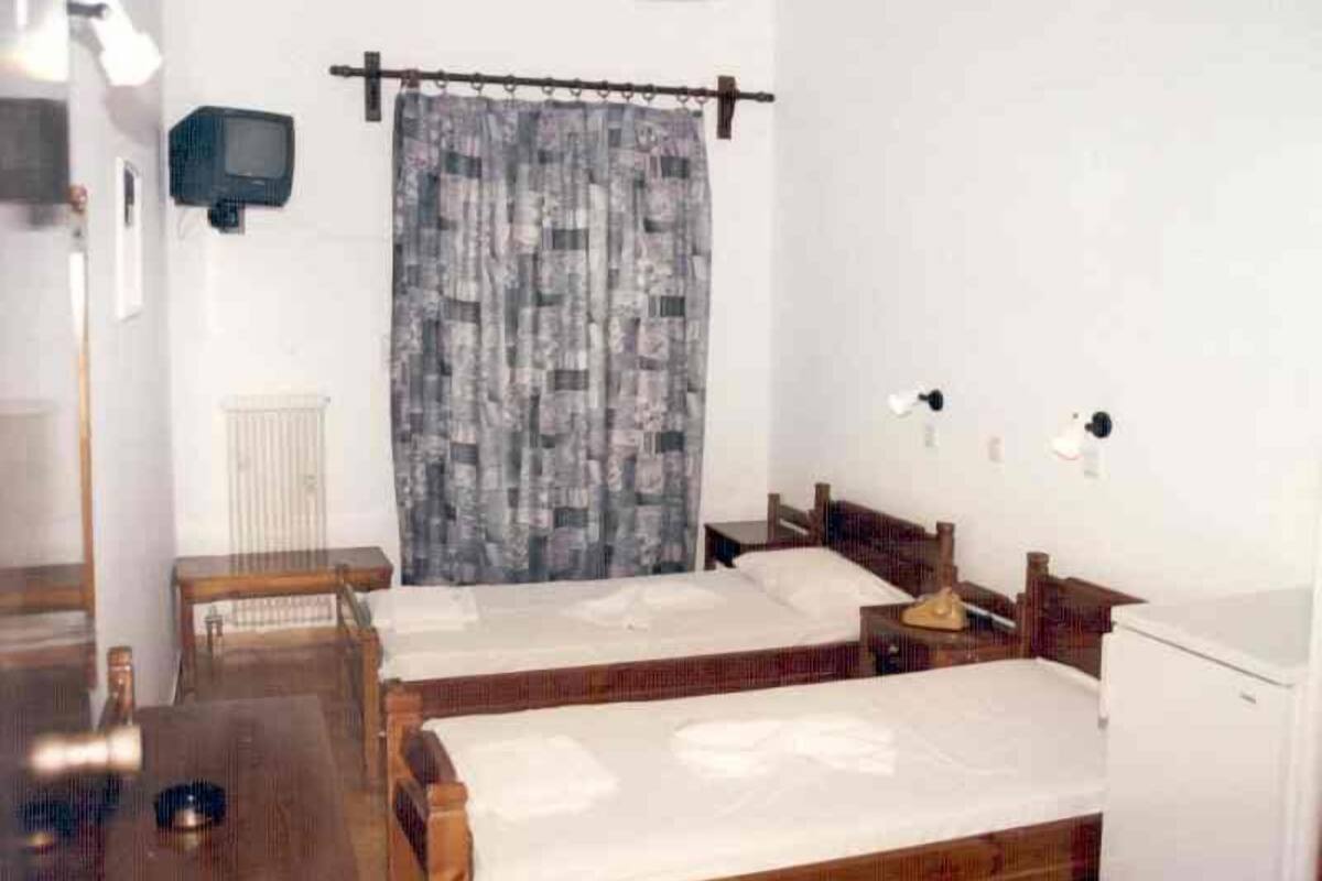 Ein Zimmer mit zwei Holzbetten, einem kleinen Tisch, einem an der Wand befestigten Fernseher und einer Heizung.