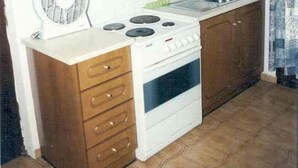 Une cuisine de taille réduite, avec des meubles en bois, un poêle blanc et un ventilateur.