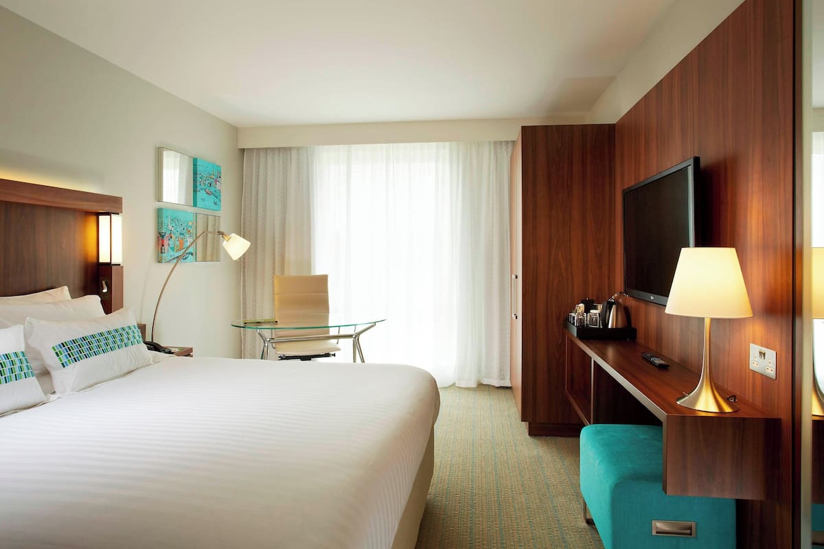 Een hotelkamer met een groot bed, een bureau met een lamp, een televisie en een raam met gordijnen.