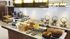 Un buffet proposant une variété de plats et de boissons, notamment des fruits, des pâtisseries et des machines à café.