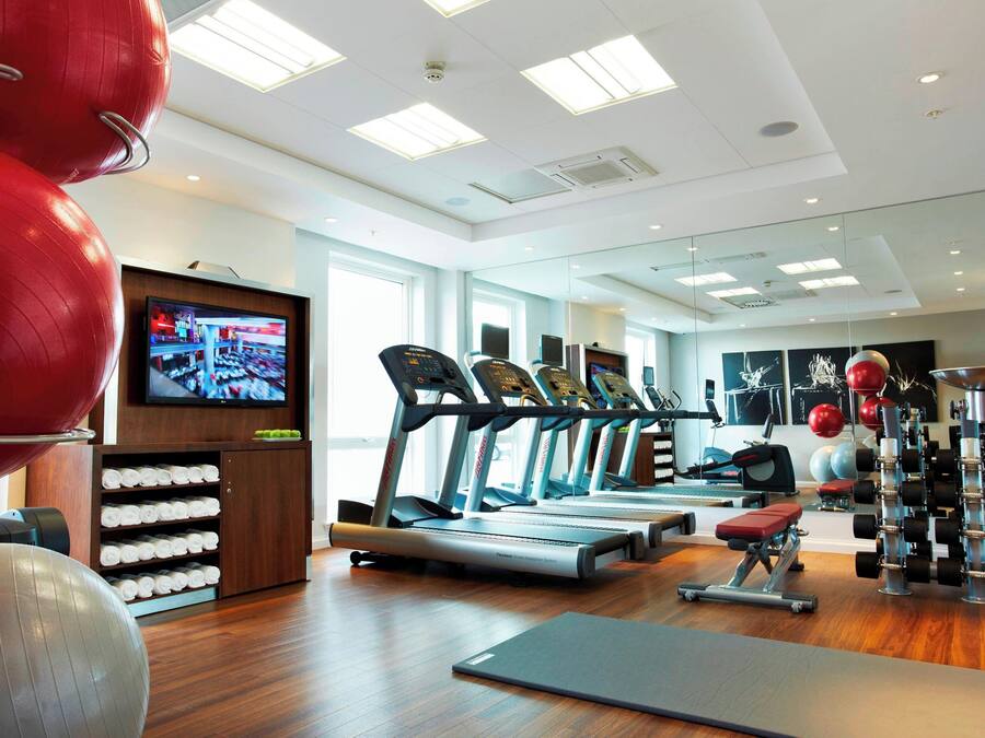 A gym with treadmills, exercise balls, and a television on the wall.