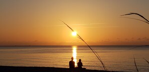 A sunset over a calm sea with two people sitting on the shore, silhouetted against the sky. - The Desoto Inns (Hollywood)