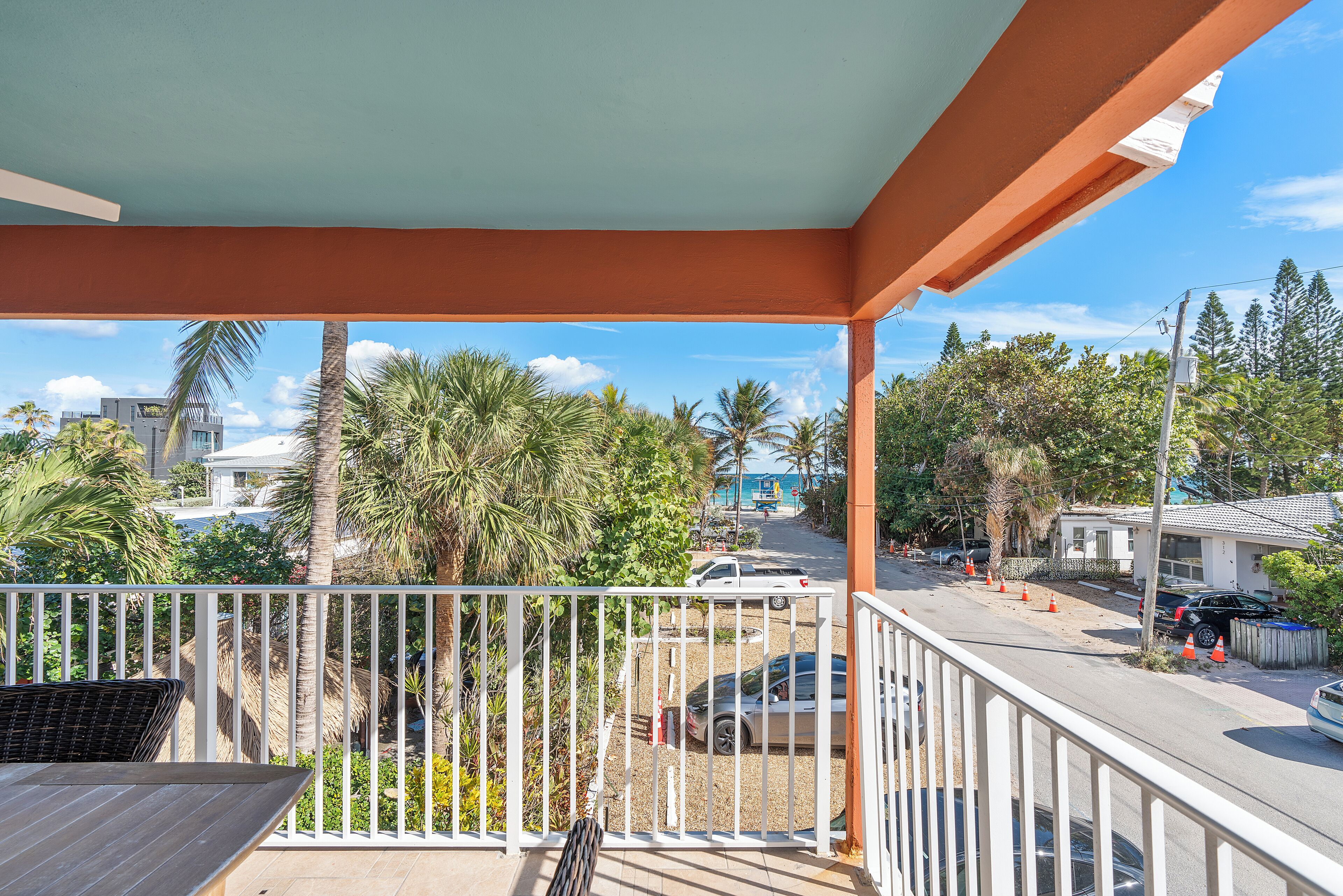 A balcony with a view of a street, palm trees, and parked cars.