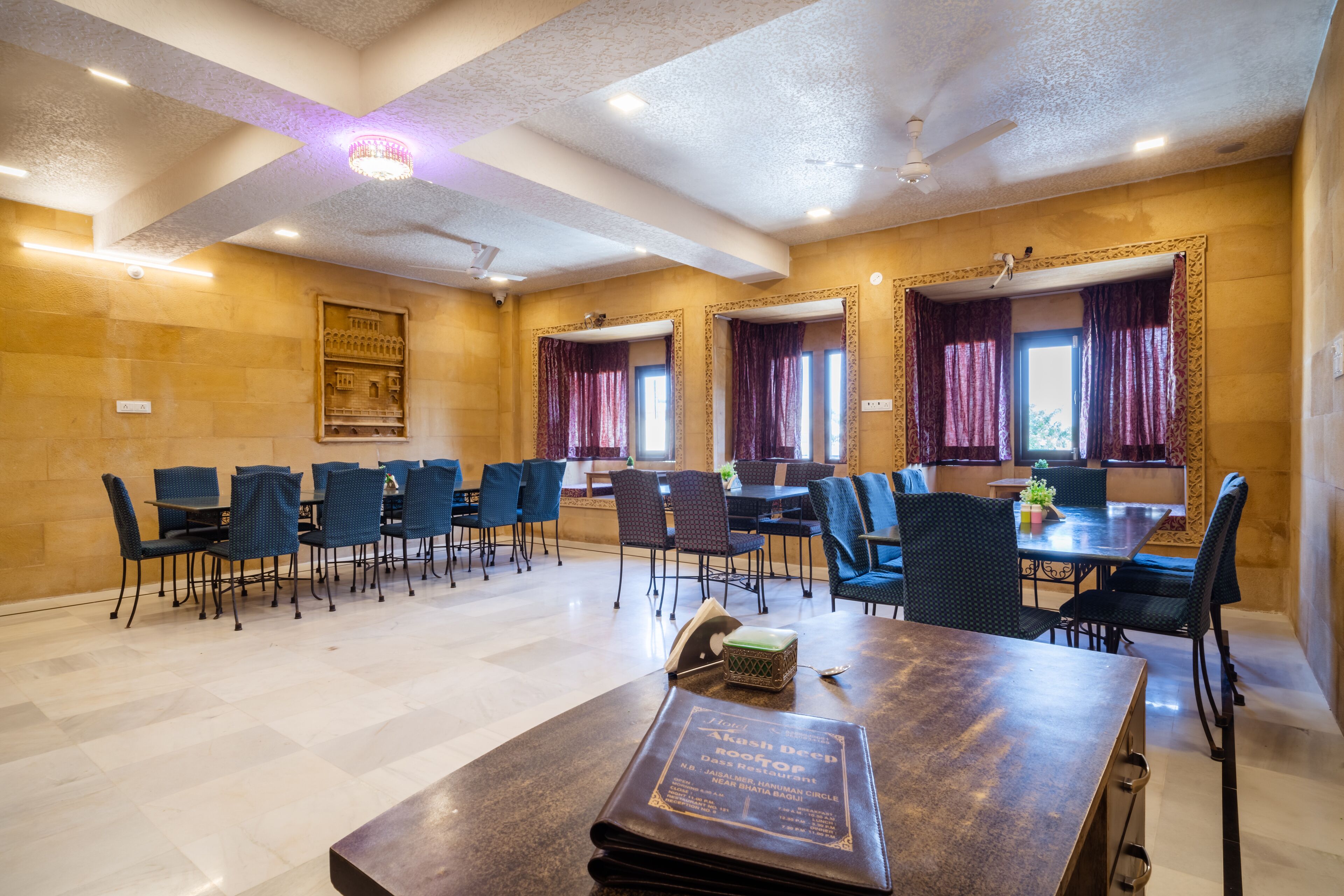 A hotel dining area with tables and chairs, a chandelier, and a ceiling fan.