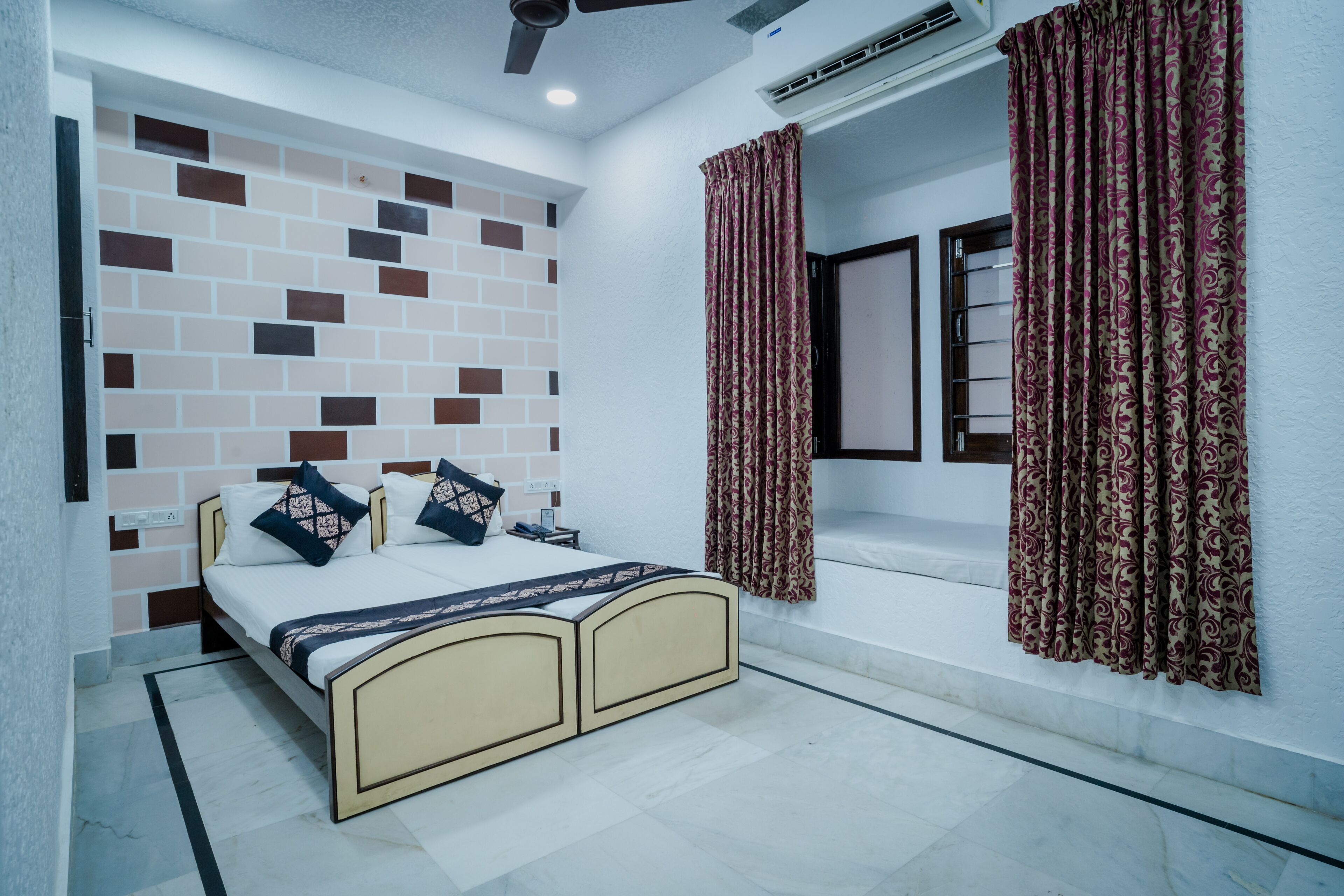 Un dormitorio con cama, aire acondicionado en la pared y cortinas estampadas.