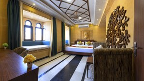 Une chambre d’hôtel avec un grand lit, un coin salon avec vue, un élément décoratif mural et un bureau agrémenté d’un vase de fleurs.