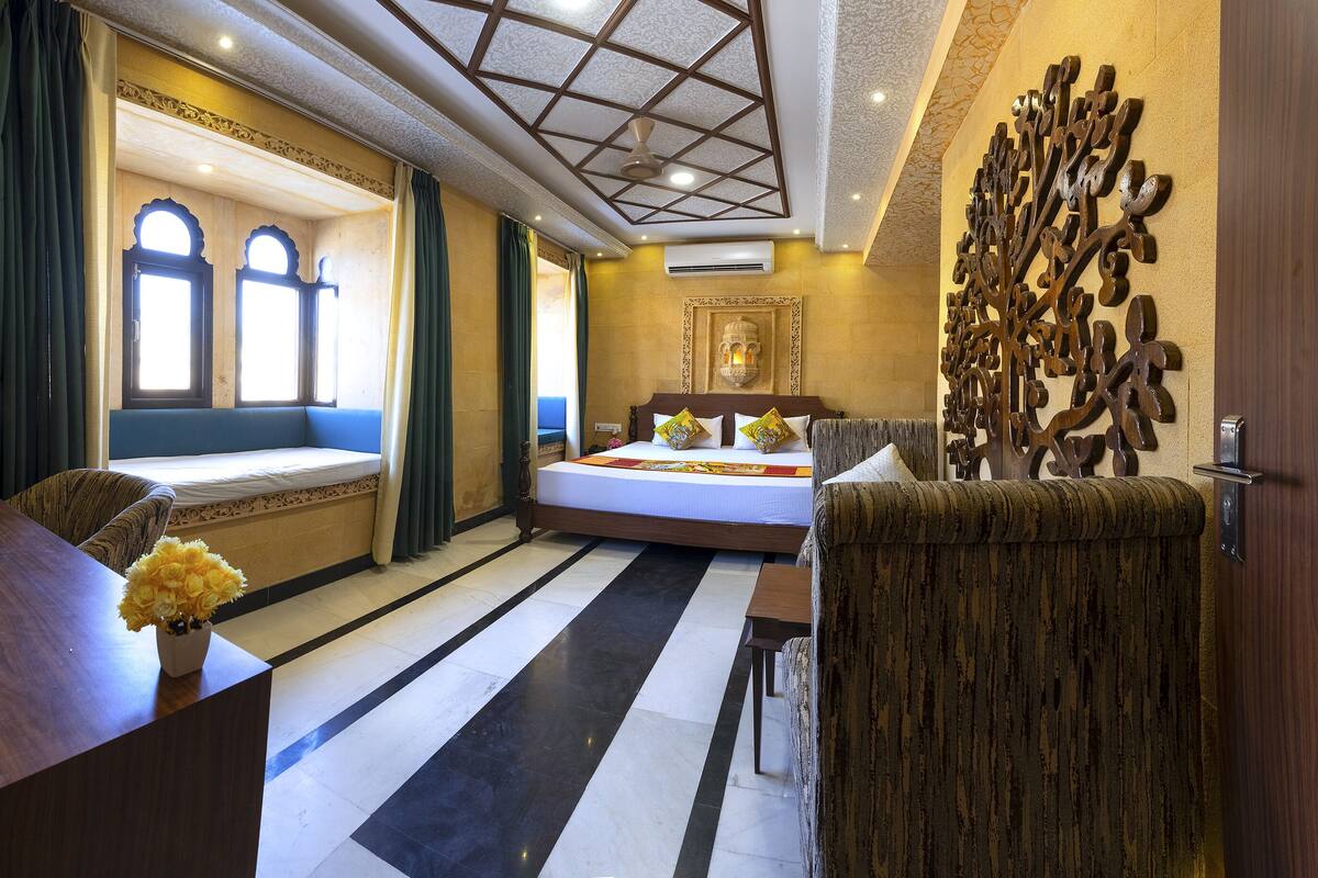 A hotel room with a large bed, a seating area with a view, a decorative wall piece, and a desk with a vase of flowers.