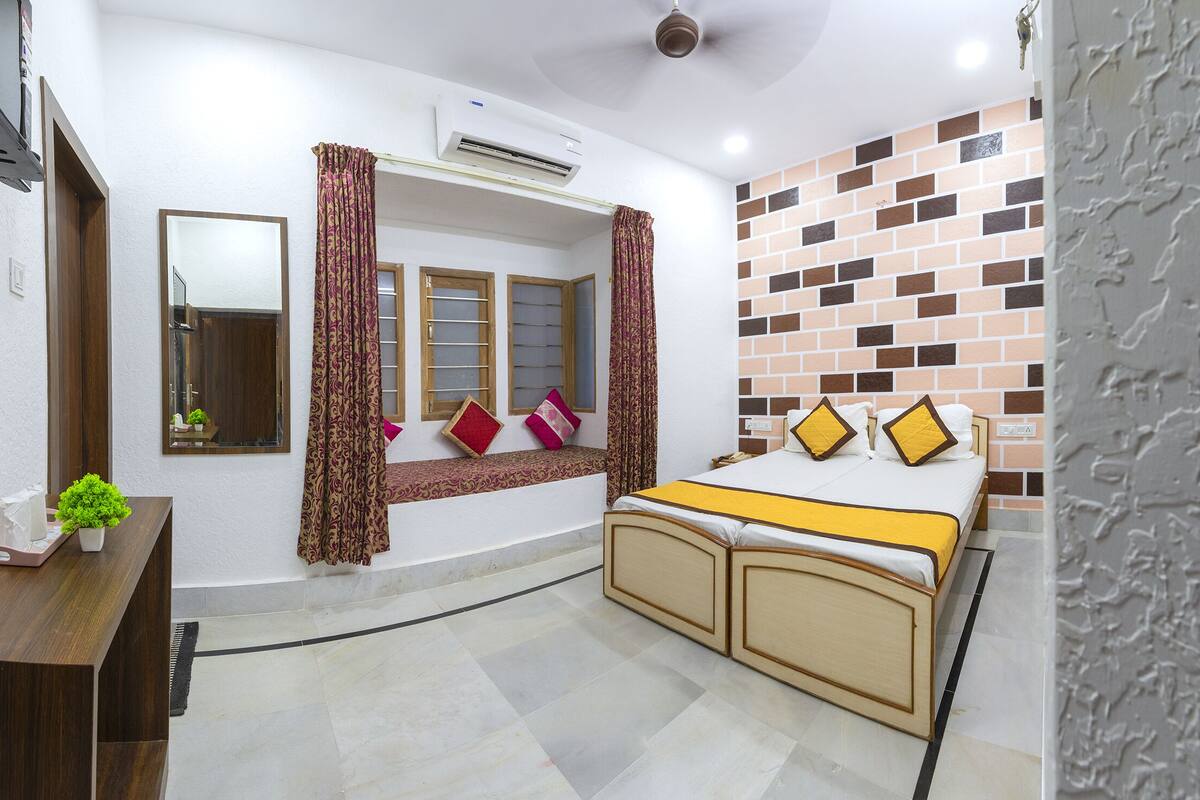 A bedroom with a bed, a bedside table, a mirror, and a window with curtains.