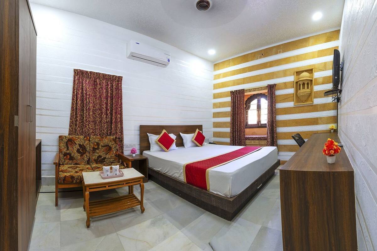A hotel room with a bed, a sofa, a small table, a desk, and a television.